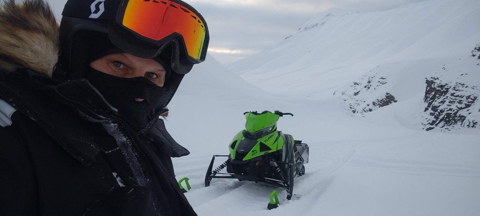 Guide in helmet and goggles beside a snowmobile in a Svalbard valley