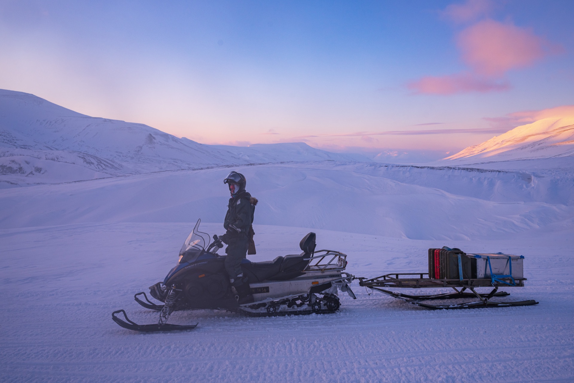 Snowmobile and sled on the fjord ice at dusk, Svalbard