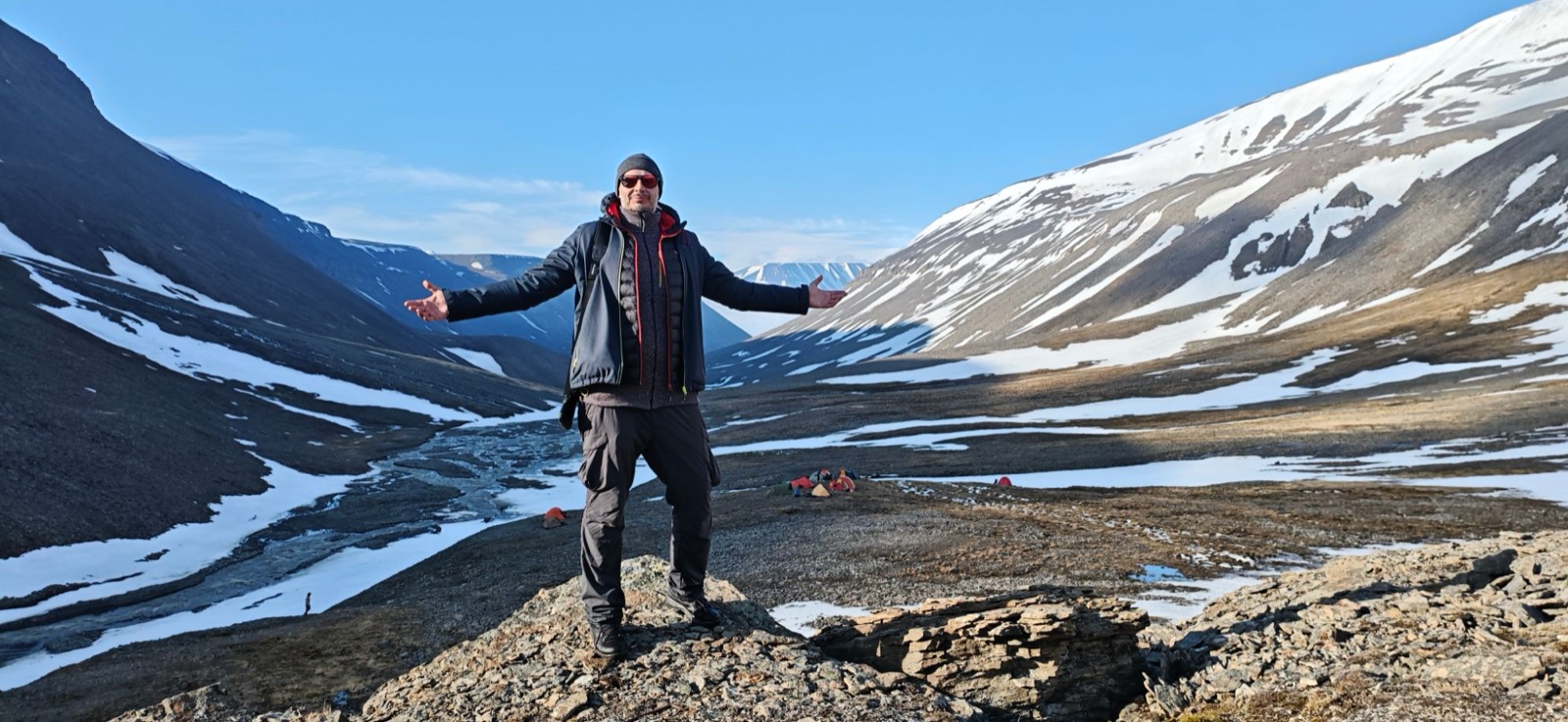 Summer valley on Svalbard with patches of snow, a meltwater river and a camp in the distance
